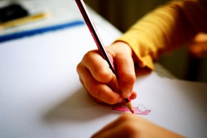 Mano di un bambino che scrive con la matita, immagine collegata a difese immunitarie bambini, ansia da prestazione scolastica e ansia per la scuola al ritorno sui banchi.
